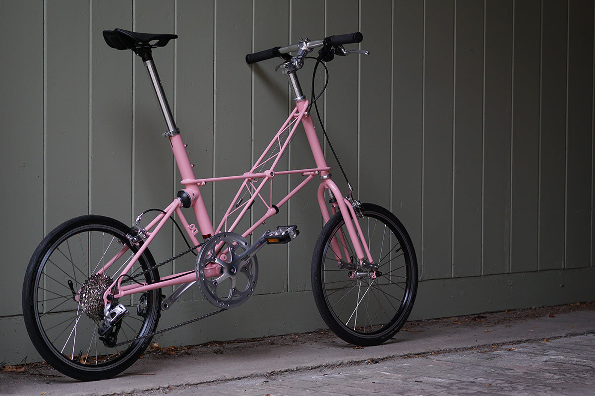 Pink Moulton bike leaning against a grey panelled wall.